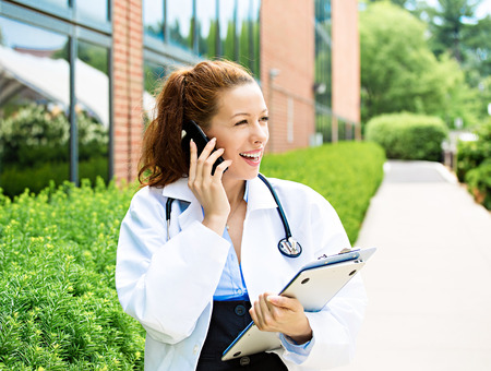 Closeup portrait, young smiling confident female doctor, healthcare professional talking on phone, giving consultation isolated background hospital campus. Patient visit health care. Positive emotionsの写真素材