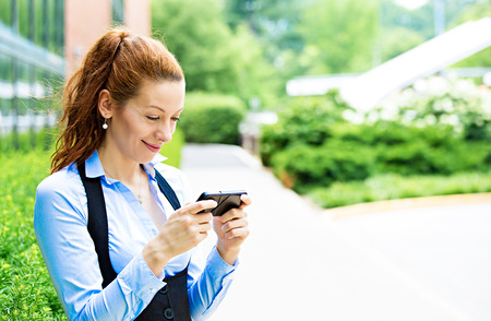 Closeup portrait happy, cheerful, girl excited by what she sees on cell phone isolated corporate office building. Facial expression reaction. Business woman sending text message from mobileの写真素材