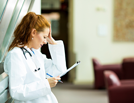 Closeup portrait sad health care professional, stressed, holding head with hand, reviewing patient chart, unhappy with diagnosis. の写真素材