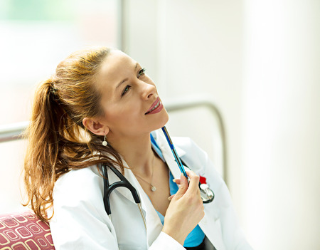 Closeup portrait, young smiling happy female doctor, healthcare professional, daydreaming, thinking isolated hospital officeの写真素材