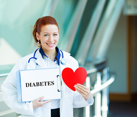 Closeup portrait happy smiling female health care professional, woman family doctor, cardiologist with stethoscope holding sign diabetes, heart isolated hospital hallway background. Patient planの写真素材