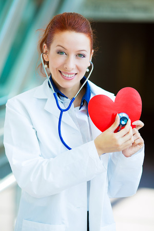 Closeup portrait smiling cheerful health care professional, pharmacist, dentist, nurse cardiologist doctor with stethoscope, holding listening heart isolated background hospital hallway. Patient visitの写真素材