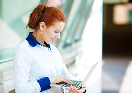 Business technology, internet hotel concept. Closeup portrait happy smiling businesswoman working on tablet pc computer checking email isolated background corporate office hallway. Positive expressionの写真素材
