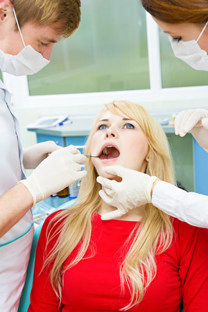 Closeup portrait young female, woman, patient sitting in dentist chair, office, opened mouth getting oral examination, procedure done by doctor, assistant isolated clinic office background equipmentの写真素材