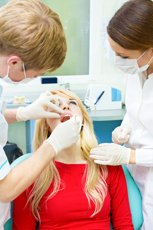 Closeup portrait young female, woman, patient sitting in dentist chair, office, opened mouth getting oral examination, procedure done by doctor, assistant isolated clinic office background equipmentの写真素材