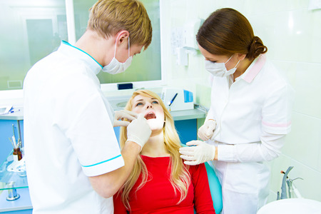 Closeup portrait young female, woman, patient sitting in dentist chair, office, opened mouth getting oral examination, procedure done by doctor, assistant isolated clinic office background equipmentの写真素材