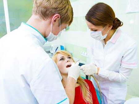 Closeup portrait young female, woman, patient sitting in dentist chair, office, opened mouth getting oral examination, procedure done by doctor, assistant isolated clinic office background equipmentの写真素材