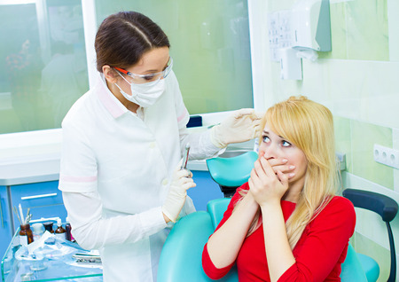 Closeup portrait terrified girl woman scared of needles, syringes, dentist visit siting in chair, opened mouth doesn't want dental procedure drilling tooth extraction isolated clinic office backgroundの写真素材