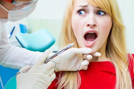 Closeup portrait terrified girl woman scared of needles, syringes, dentist visit siting in chair, opened mouth doesn't want dental procedure drilling tooth extraction isolated clinic office backgroundの写真素材