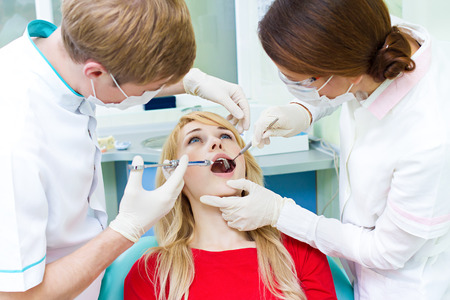 Closeup portrait young female, woman patient sitting in dentist chair, office with wide open mouth getting painful anesthetic injection done by doctor, his assistant isolated background clinic officeの写真素材
