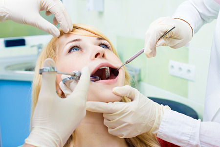 Closeup portrait young female, woman patient sitting in dentist chair, office with wide open mouth getting painful anesthetic injection done by doctor, his assistant isolated background clinic officeの写真素材