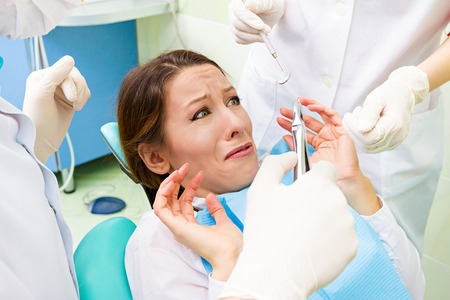 Closeup portrait young terrified girl woman scared at dentist visit, siting in chair, funny looking with fear, doesn't want dental procedure drilling tooth extraction isolated clinic office backgroundの写真素材