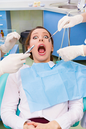 Closeup portrait young terrified girl, woman scared at dentist visit, siting in chair, wide open mouth, doesn't want dental procedure, drilling, tooth extraction, isolated clinic office backgroundの写真素材