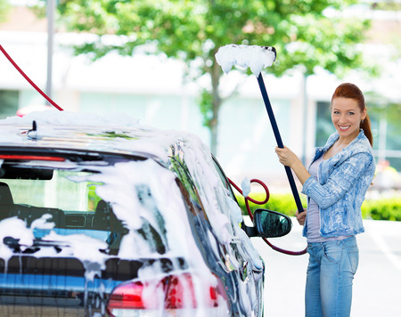 Picture, portrait young, smiling, happy, attractive woman washing automobile at manual car washing self service station, cleaning with foam, pressured water. Transportation, auto, vehicle care conceptの写真素材