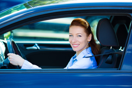 Portrait smiling, attractive brunette woman, buckled up, driving, testing her new black car, automobile, purchased at dealership, isolated street, city traffic background. Safe driving habits conceptの写真素材