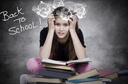Closeup portrait young little girl, stressed tired fatigued upset, sitting on pile of books, isolated dark grey black background.の写真素材