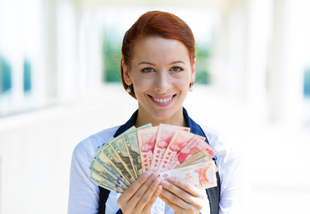 Closeup portrait happy excited successful business woman holding money dollar bills, currency from different countries in hand, isolated corporate office background. Positive emotion, face expressionの写真素材