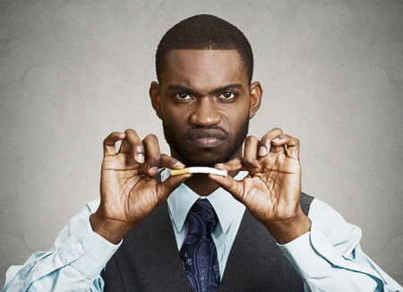 Closeup portrait, headshot, young, handsome, unhappy, angry  business man, corporate executive breaking cigarette, isolated black grey background. Life style changes. Human face expressions, emotionsの写真素材
