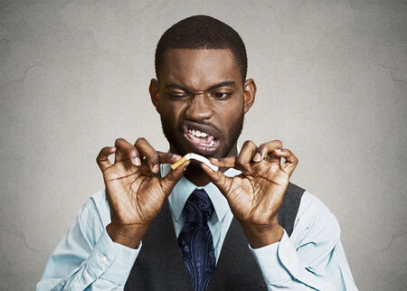 Closeup portrait, headshot, young, handsome, unhappy, angry  business man, corporate executive breaking cigarette, isolated black grey background. Life style changes. Human face expressions, emotionsの写真素材