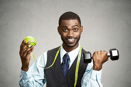 Closeup portrait, headshot business man, corporate executive holding green apple dumbbell, measuring tape on neck isolated black grey background. Healthy life style concept. Positive face expressionの写真素材