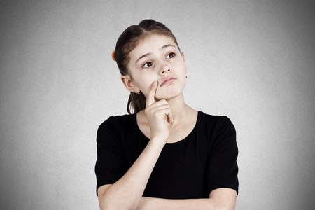 Closeup portrait, serious pensive little girl touching her cheek, thinking, daydreaming about something, looking up, isolated dark grey background. Human face expressions, emotions, reaction, feelingsの写真素材