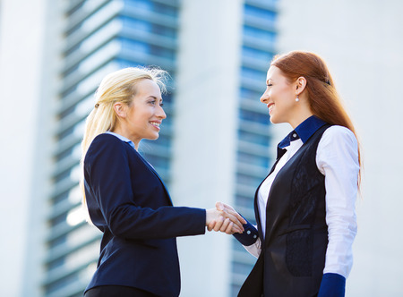 Closeup portrait happy smiling businesspeople, attractive business women shaking hands outdoor, isolated background corporate office, building background. Positive face expressions, emotions, attitudeの写真素材
