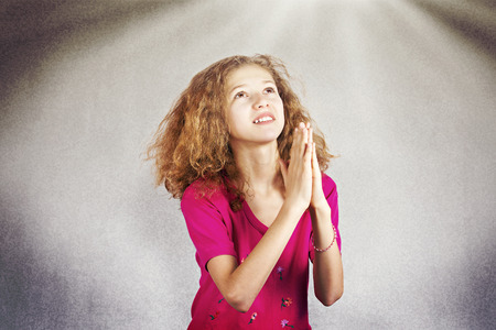 Closeup portrait young girl praying, eyes opened, looking up, hoping for best, asking  forgiveness, miracle, help isolated sky light background. Positive human emotions, facial expressions, feelingsの写真素材