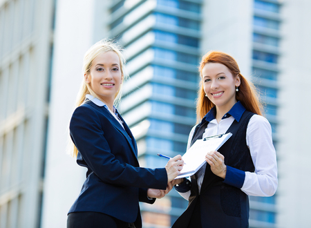 Closeup portrait two smiling young business women, company employees signing contract document, agreement paper, paperwork isolated corporate office background. Positive human face expression, emotionの写真素材