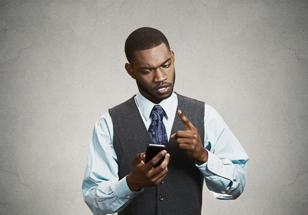 Closeup portrait angry young business man, guy, mad worker, pissed off employee while on mobile, pointing with finger at his smart phone isolated black background. Negative emotions, facial expressionの写真素材