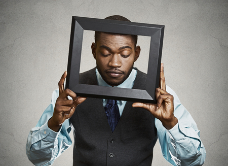Closeup portrait businessman, executive looking down curious, surprised confused through black picture frame thinking beyond borders accepted rules isolated grey background. Face expressions, emotionの写真素材