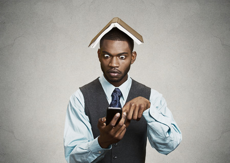 Closeup portrait surprised business man, executive reading, browsing news on smart phone holding mobile, book over head isolated black background  Human face expression, emotion, corporate lifestyleの写真素材