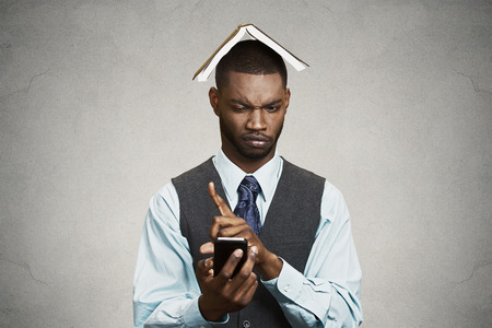 Closeup portrait upset, angry business man, funny looking corporate executive reading e-mail on smart phone, book over head isolated black background  Human face expression, emotion body languageの写真素材