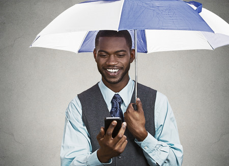 Closeup portrait happy, smiling corporate business man, executive reading message news on smart phone holding umbrella, protected from rain isolated black background  Human face expression, emotionの写真素材
