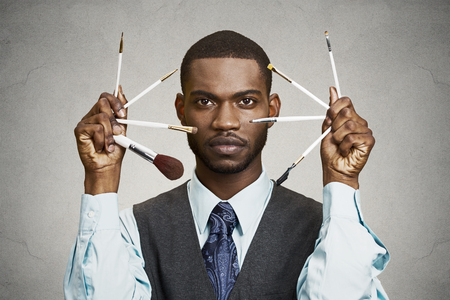 Closeup portrait headshot handsome business man, corporate executive holding make-up brushes by his face isolated black background. Human face expression emotion body language life perception attitudeの写真素材