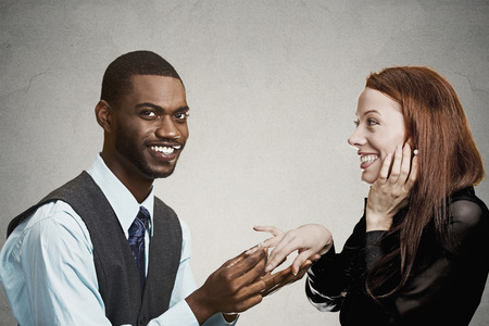 Closeup portrait couple, handsome happy man proposing to excited smiling young woman isolated grey black background. Holidays, love, relationship dating concept. Human face expression emotion feelingsの写真素材
