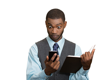 Closeup portrait surprised shocked business man executive reading breaking news on smart phone holding book isolated white background. Human face expression, emotion, corporate company lifestyle の写真素材