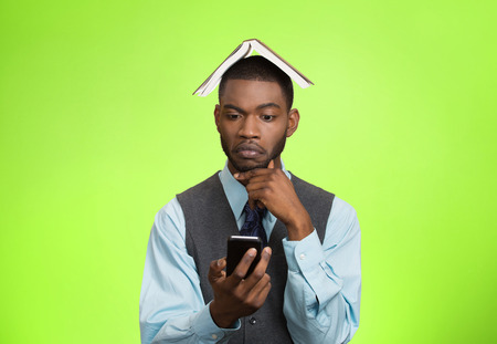 Closeup portrait business man corporate executive thinking how to reply to message on smart phone holding mobile, book over head isolated green background.の写真素材