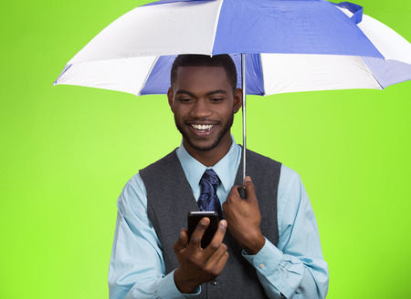 Closeup portrait happy, smiling corporate business man, executive reading message news on smart phone holding umbrella, protected from rain isolated green background.の写真素材