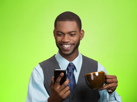 Closeup portrait happy, smiling business man reading good news on smart phone, lawyer holding mobile, drinking cup coffee isolated green background. の写真素材