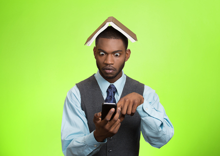 Closeup portrait surprised business man, executive reading, browsing news on smart phone holding mobile, book over head isolated green background. の写真素材