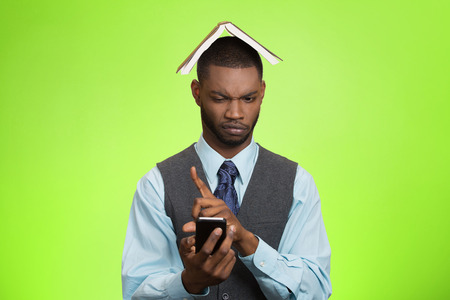 Closeup portrait upset, angry business man, funny looking corporate executive reading e-mail on smart phone, book over head isolated green background. Human face expression, emotion body language の写真素材