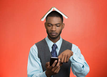 Closeup portrait serious business man, executive reading replying to message on smart phone holding mobile, book over head isolated red background. Human face expression, emotion corporate lifestyle の写真素材
