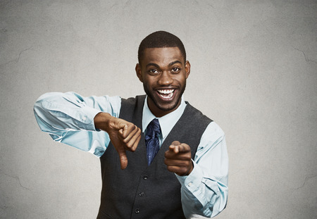 Closeup portrait sarcastic young man showing one thumbs down sign hand gesture, happy that someone made mistake, lost, failed isolated black background. Negative emotions, facial expressions, feelingsの写真素材