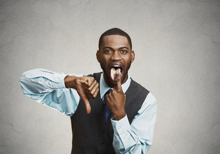Closeup portrait, young unhappy, annoyed, rude man putting finger in mouth showing something sucks with thumbs down, isolated black background. Negative human emotions, feelings, facial expressionsの写真素材