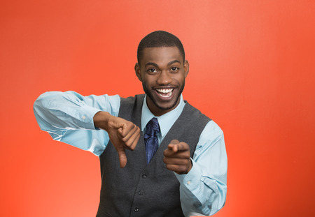 Closeup portrait sarcastic young man showing one thumbs down sign hand gesture, happy that someone made mistake, lost, failed isolated red background. Negative emotions, facial expressions, feelingsの写真素材
