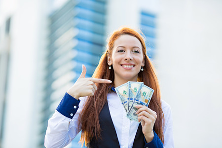 Closeup portrait super happy excited successful young business woman holding money dollar bills in hand isolated corporate office background. Positive emotion face expression feeling. Financial rewardの写真素材
