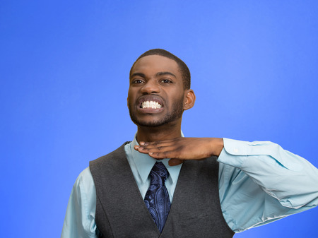 Closeup portrait, angry, mad young executive man gesturing with hand to stop talking, cut it out, or he will take your head off, isolated blue background. Negative emotion, facial expression feelingsの写真素材