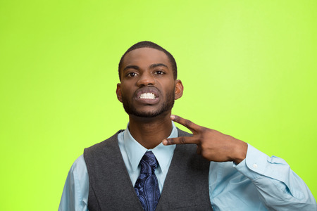 Closeup portrait, angry, mad young executive man gesturing with hand to stop talking, cut it out, or he will take your head off, isolated green background. Negative emotion, facial expression feelingsの写真素材