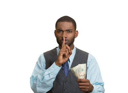 Closeup portrait handsome corrupt guy businessman holding dollar bill in hand showing shhh sign finger to lips isolated white background. Bribery concept politics, business diplomacy. Face expressionの写真素材