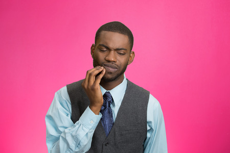 Closeup portrait handsome sad young executive man, student, worker touching face having bad pain, tooth ache, isolated pink background. Negative human emotions, facial expressions, feeling reactionの写真素材